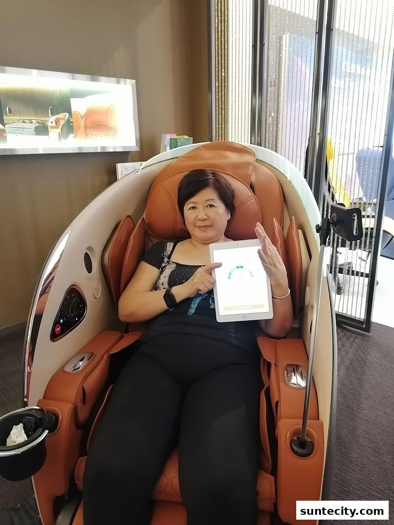 A woman sits in a massage chair, holding a tablet displaying a health-related interface.