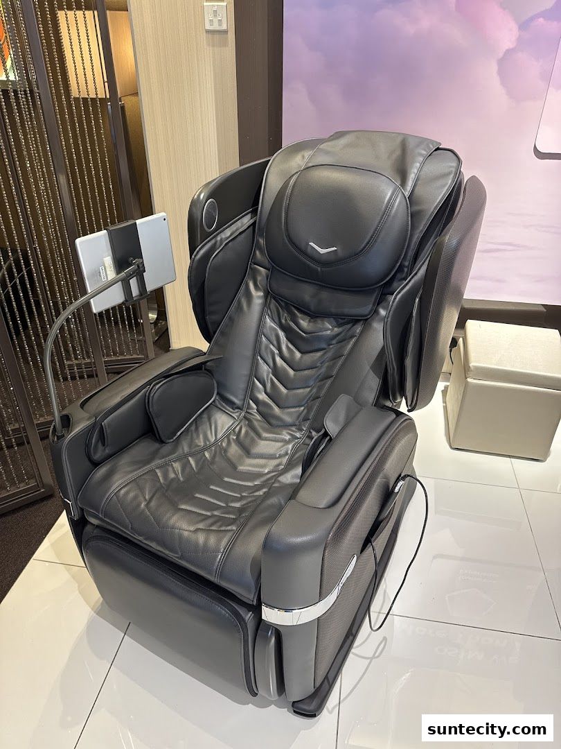 A luxurious black massage chair with a tablet holder is displayed in a well-lit retail space.