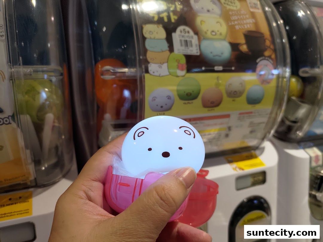 A hand holds a glowing, round character toy from a gachapon machine at Otaku House.