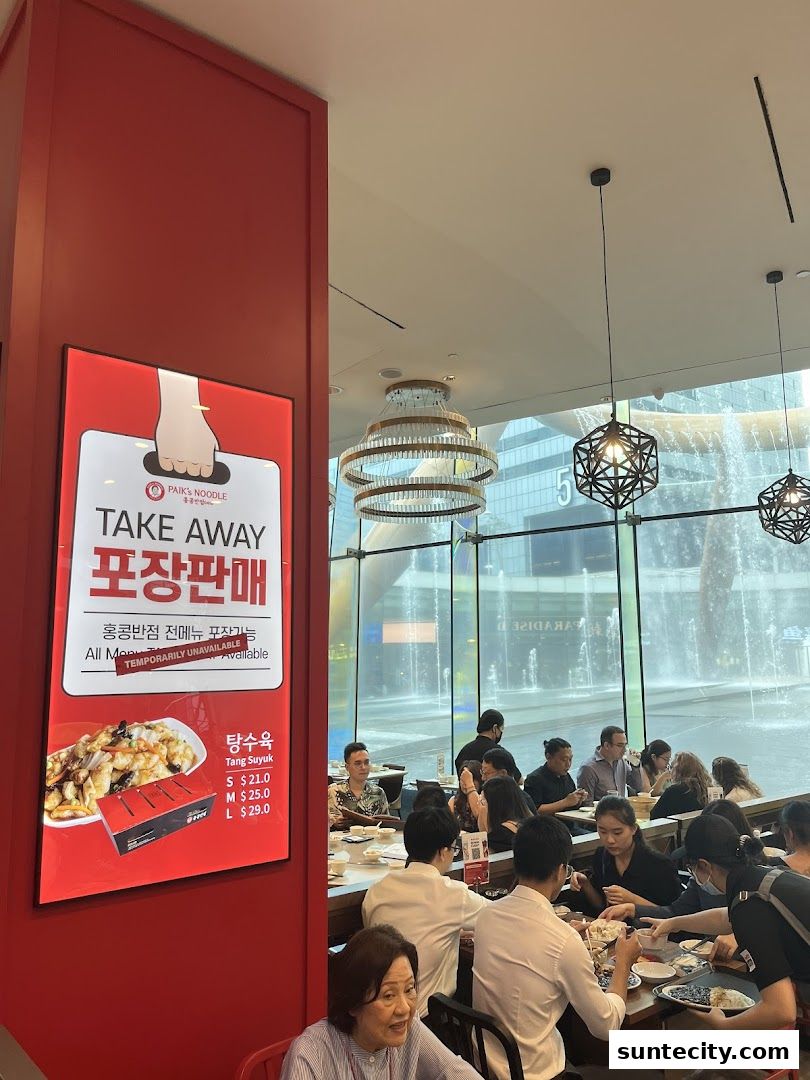 A sign for Paik's Noodle's take away service is displayed next to diners eating inside.