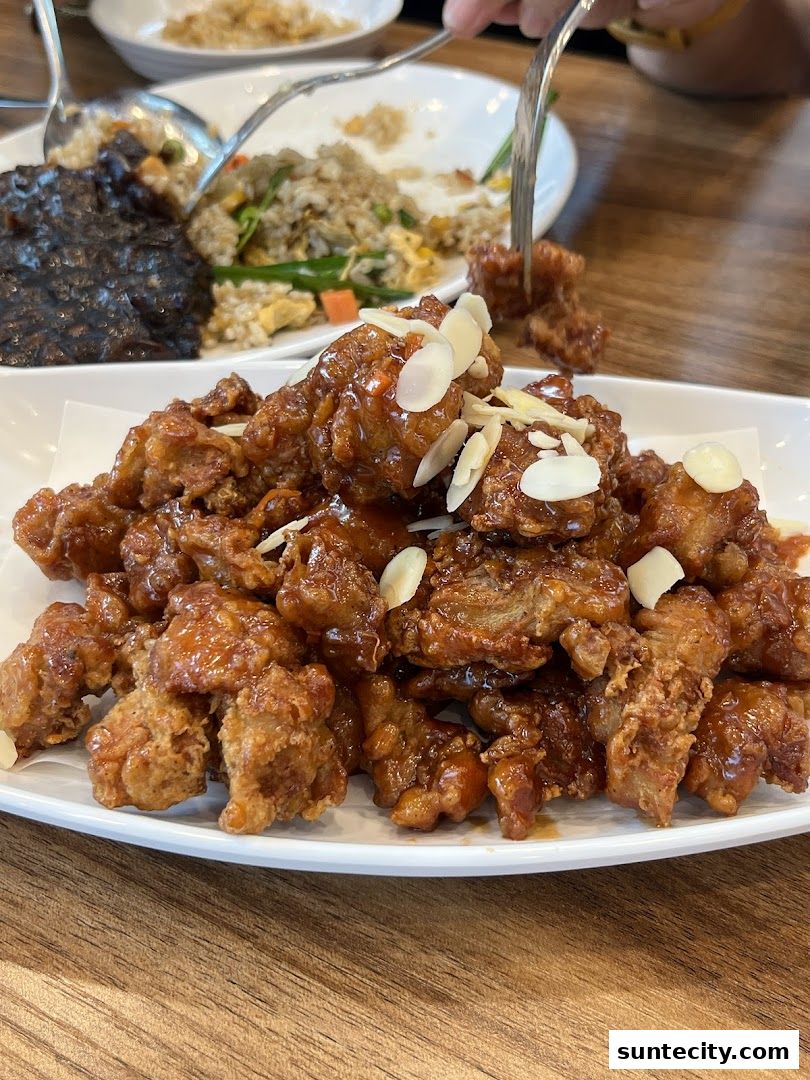 A plate of crispy fried chicken glazed with a sweet sauce and topped with sliced almonds.