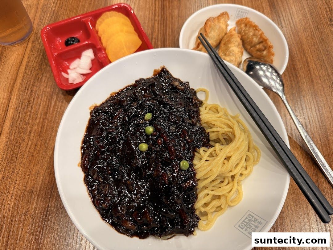 A bowl of Jajangmyeon with side dishes and dumplings on a wooden table.