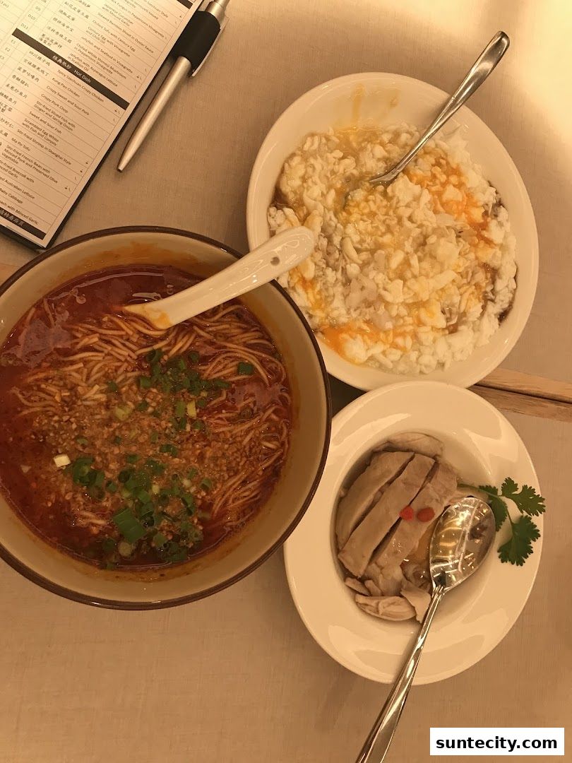A table setting with three bowls of food and a menu, featuring noodles, chicken, and a tofu dish.