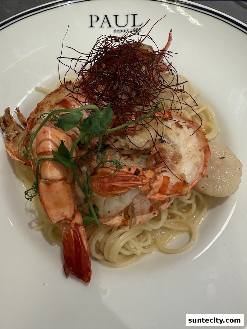 A plate of pasta with large prawns and a scallop, garnished with red threads.