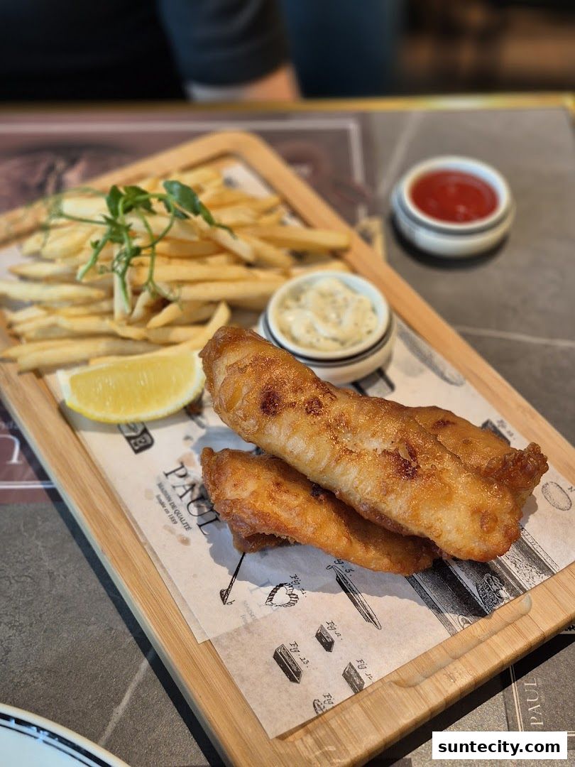 A delicious plate of fish and chips served with lemon, tartar sauce, and ketchup.