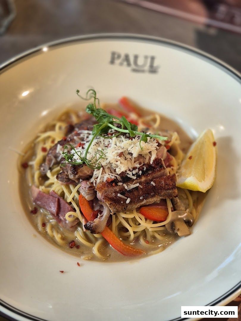 A close-up of a delicious pasta dish with sliced meat, vegetables, and a lemon wedge.