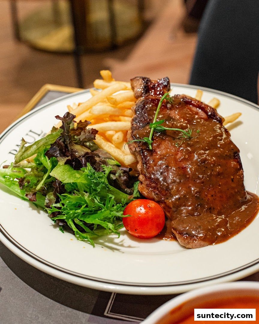 A juicy steak with fries and salad is served on a white plate with the PAUL logo.