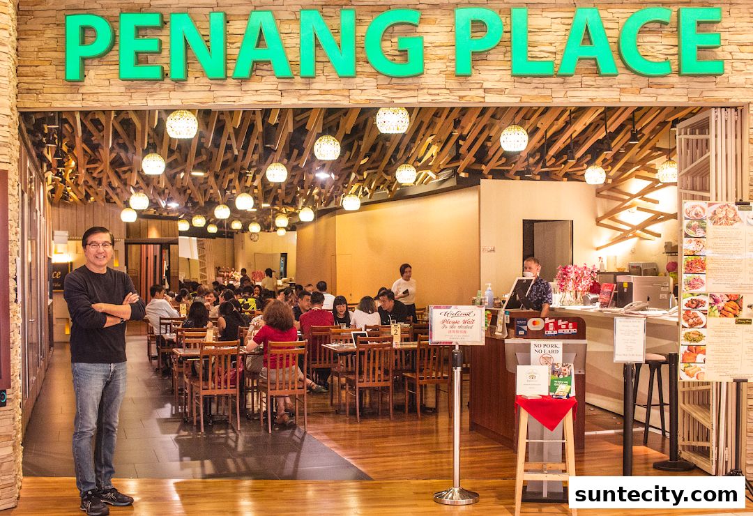 A man stands in front of Penang Place restaurant, with diners seated inside.