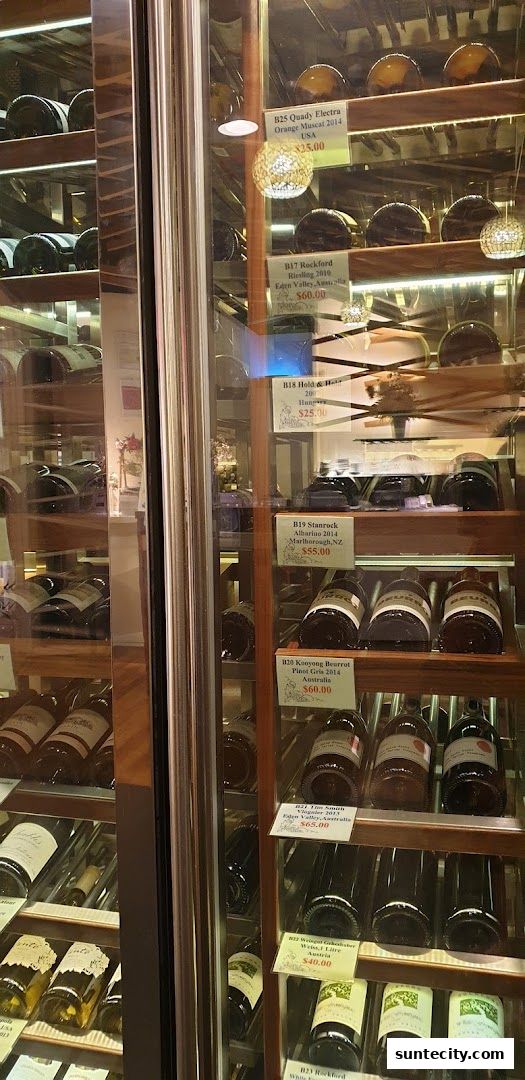 A refrigerated display case filled with bottles of wine, with labels indicating variety and price.