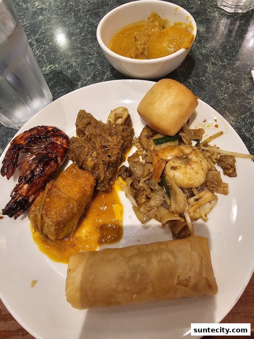 A plate of Malaysian food including grilled shrimp, curry, and spring rolls.