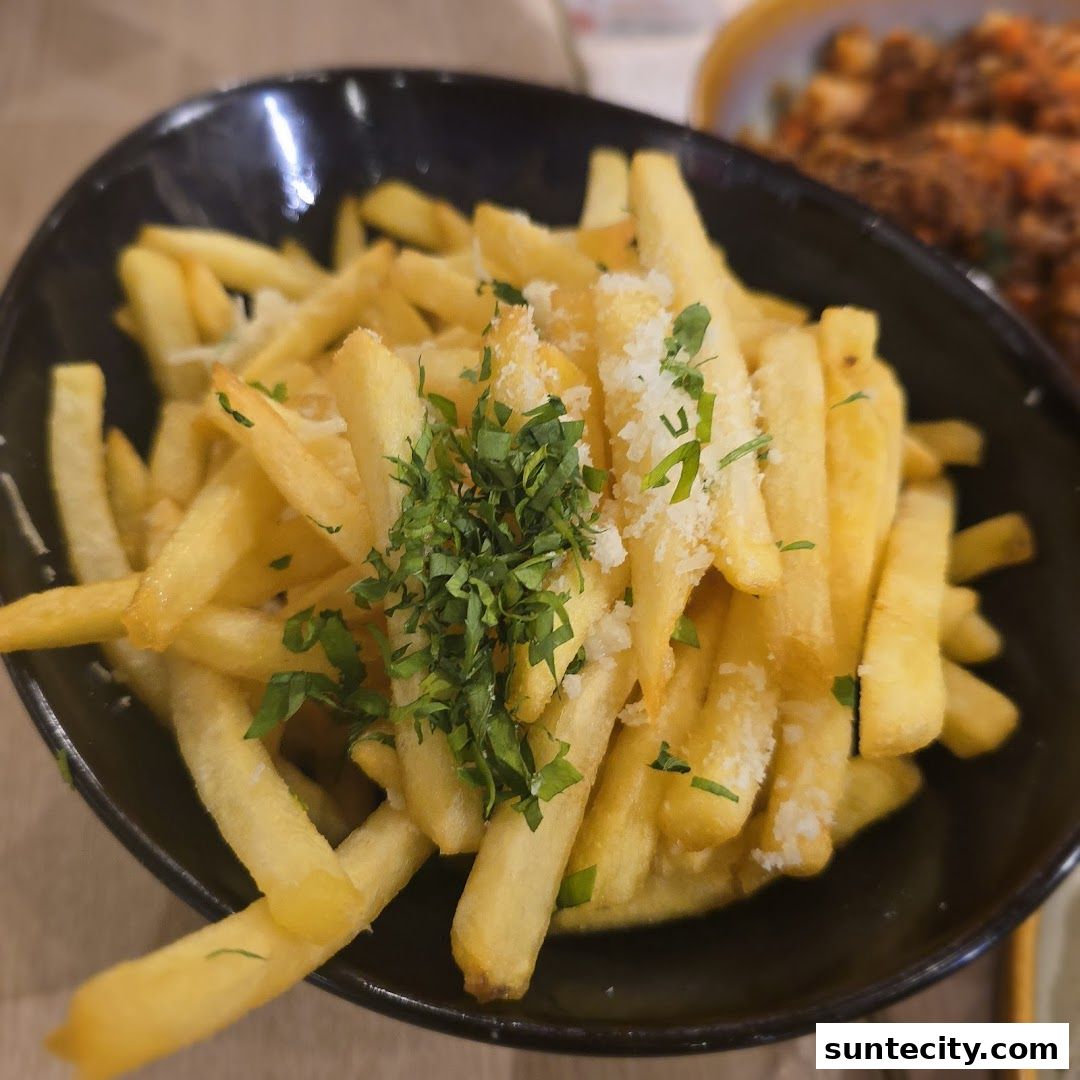 A close-up shot of a bowl of crispy french fries topped with fresh parsley and grated cheese.