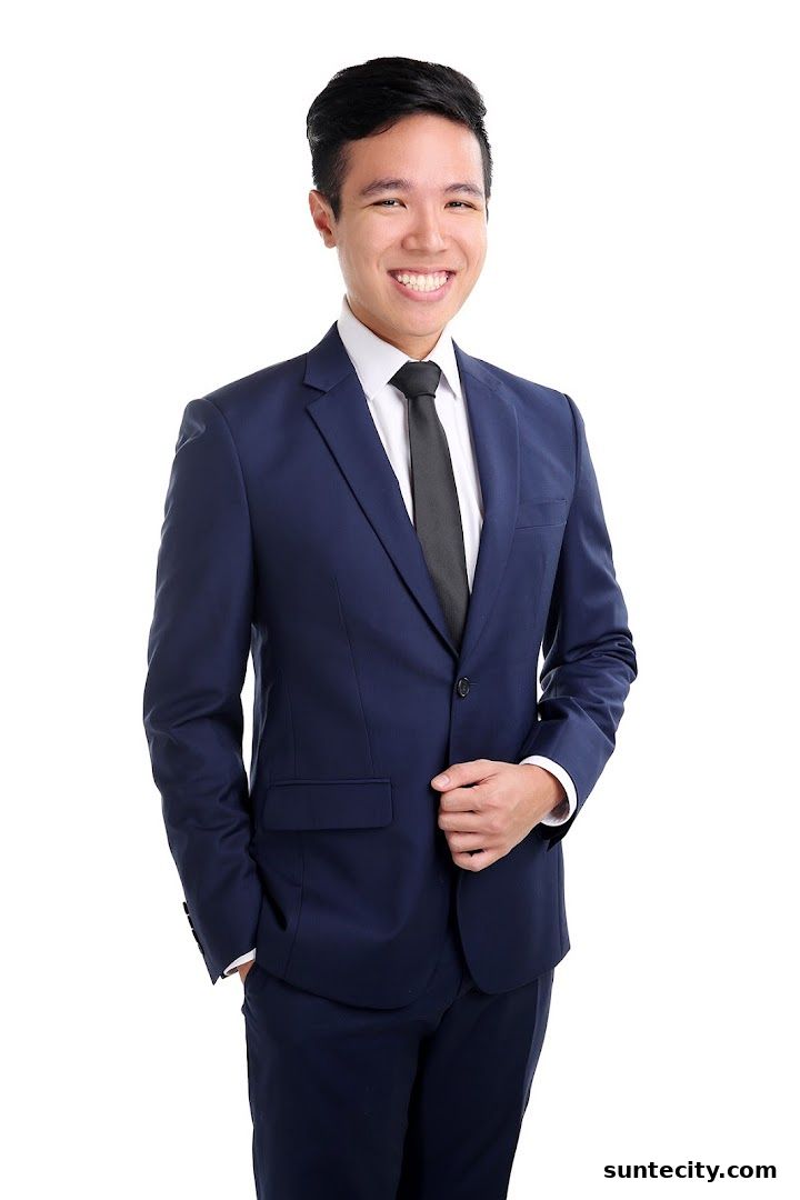 A smiling young man in a navy blue suit and white shirt with a black tie.