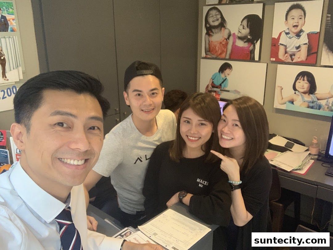 A group of four smiling people posing for a selfie in a studio with children's photos on the wall.