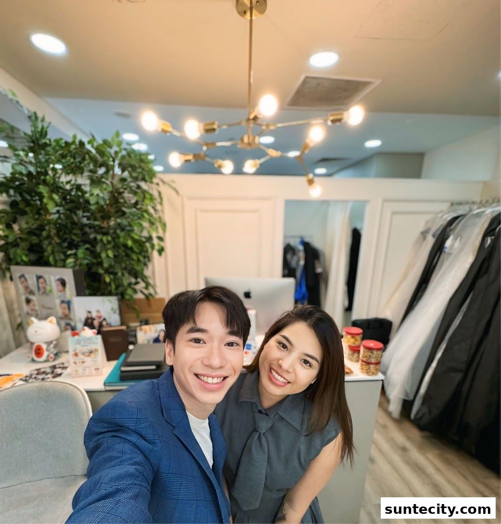 A smiling couple poses for a selfie in a shop with dresses on racks and a desk with photos.