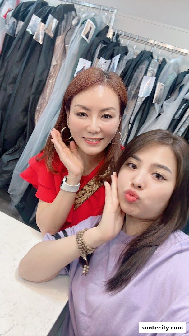 Two women smiling and posing in front of racks of dresses.