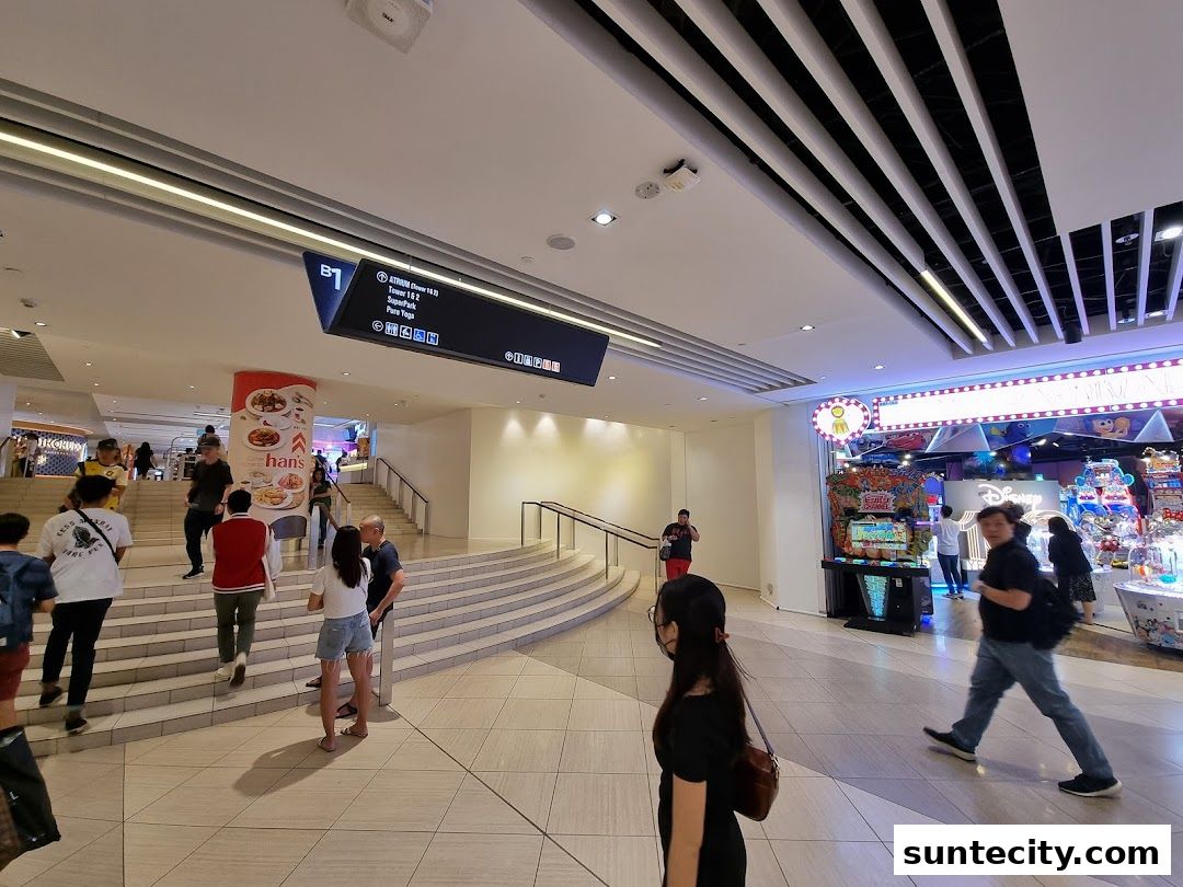 People walking in a modern shopping mall with escalators and shops visible.