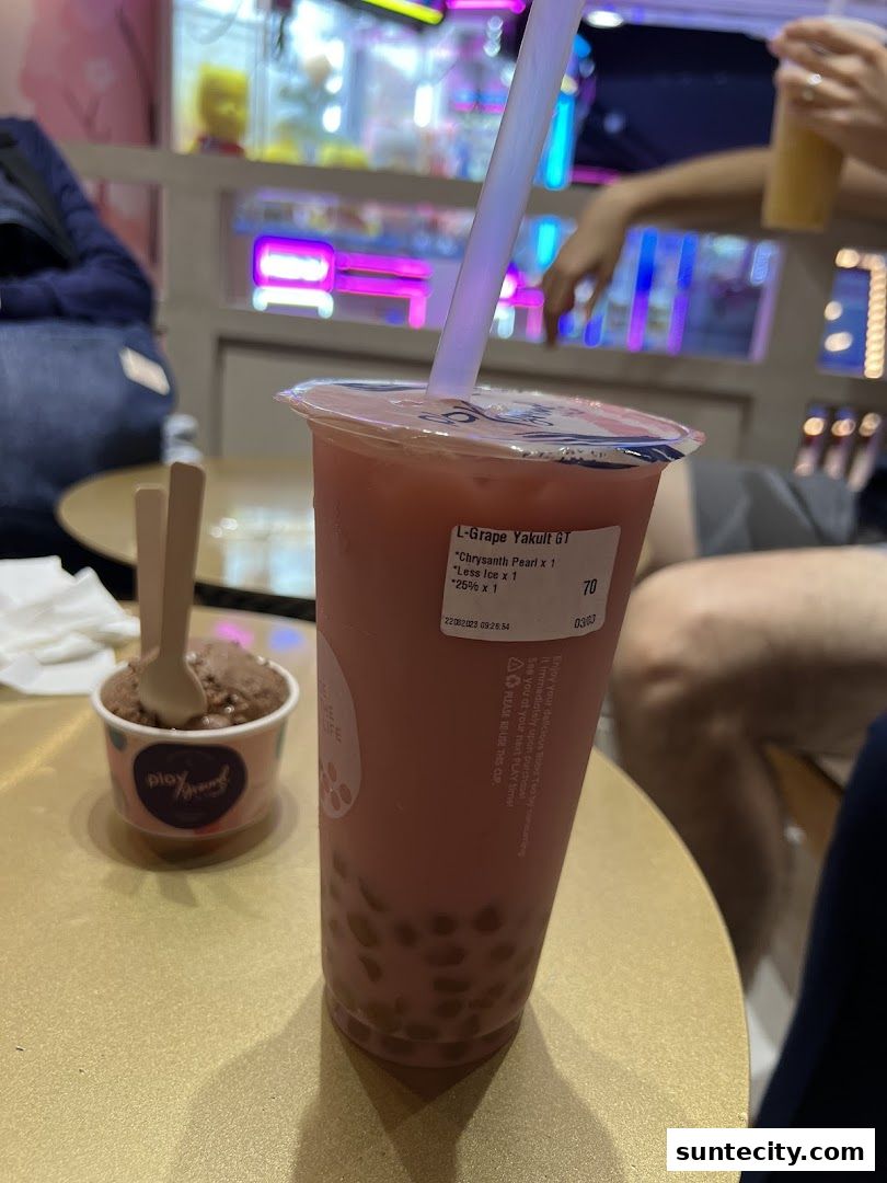 A close-up of a pink bubble tea with boba and a small cup of ice cream.