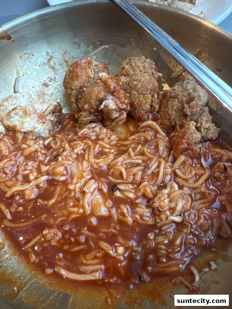 A close-up of Korean street food with fried chicken and noodles in a savory sauce.