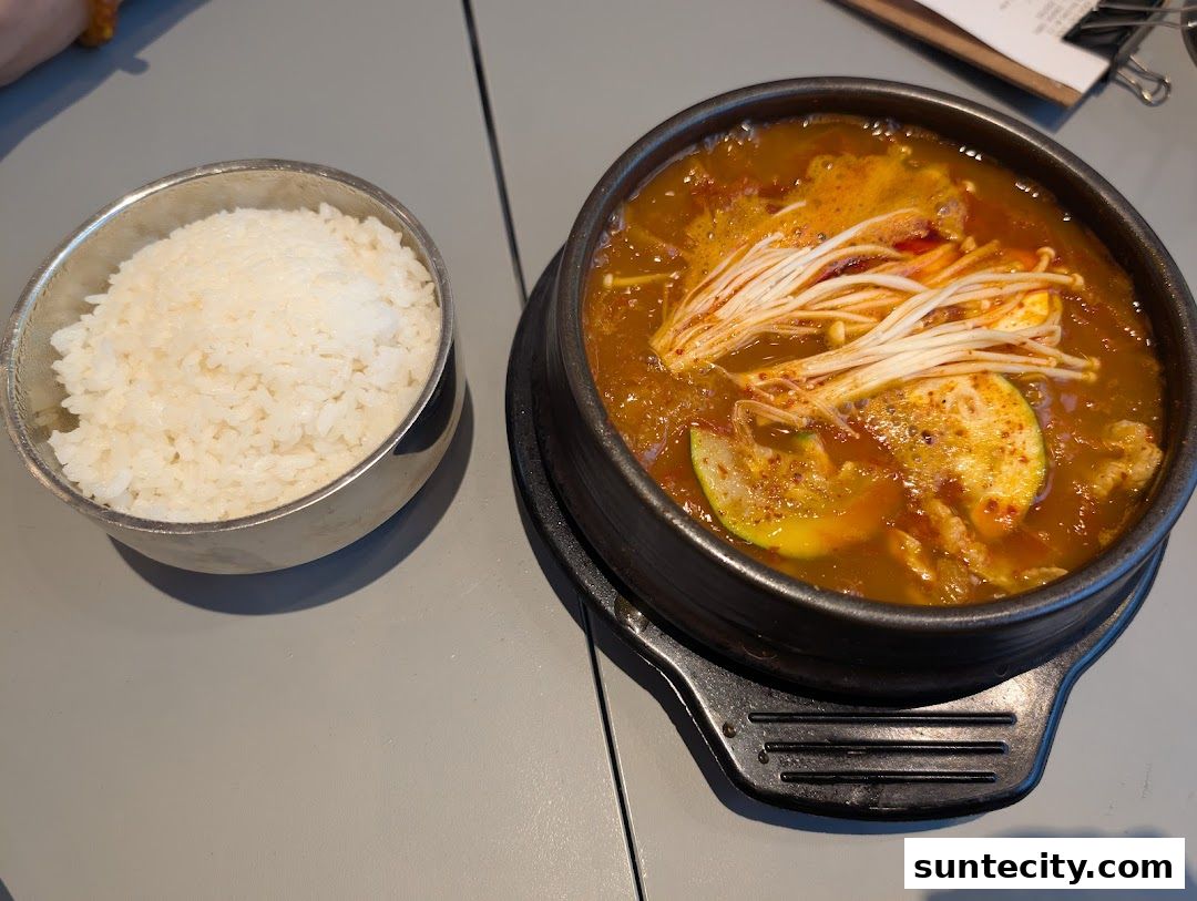 A steaming bowl of Korean stew with enoki mushrooms and rice.