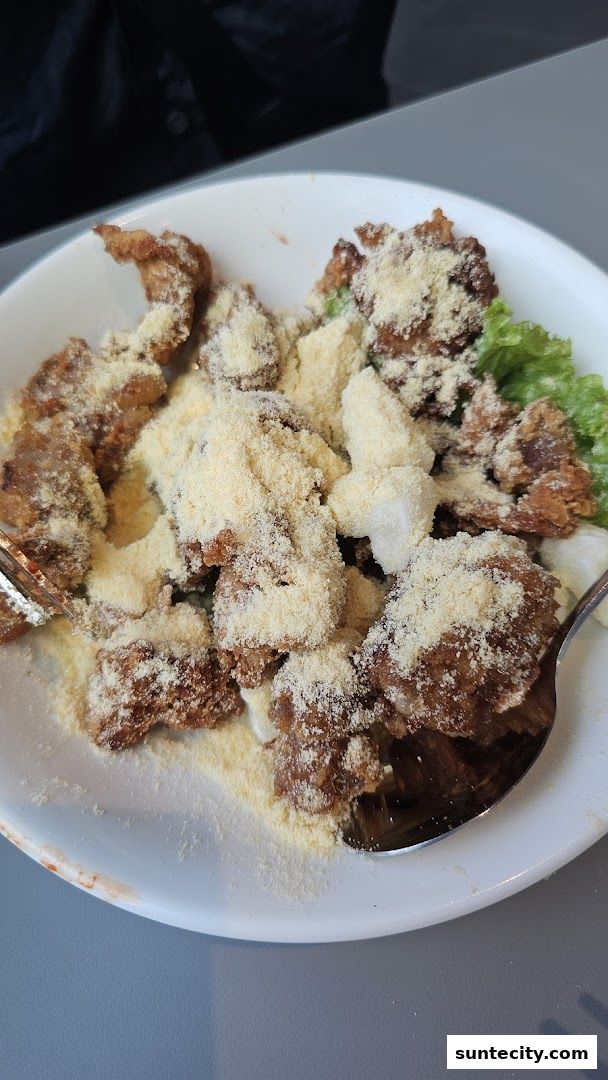 A close-up shot of a bowl of Korean fried chicken topped with cheese powder and lettuce.