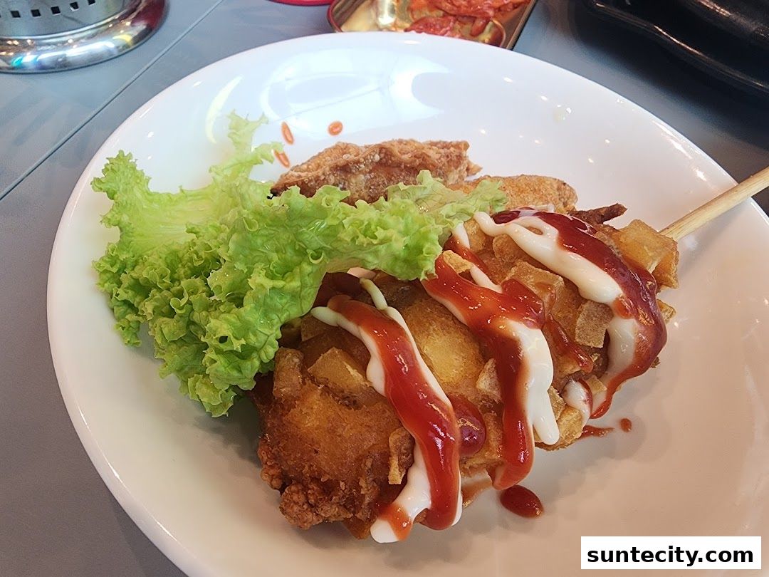 A close-up of a Korean street food item, likely a corn dog, on a white plate with lettuce.