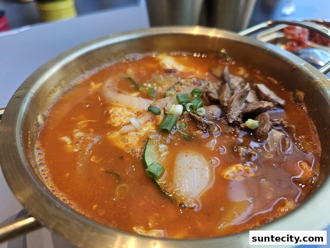 A close-up of a steaming Korean stew with meat, vegetables, and egg in a brass bowl.