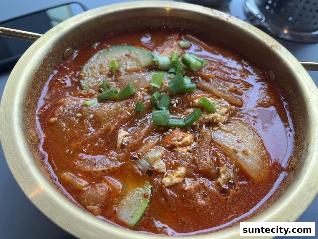 A close-up of a steaming bowl of Korean Kimchi Jjigae with kimchi, zucchini, and scallions.