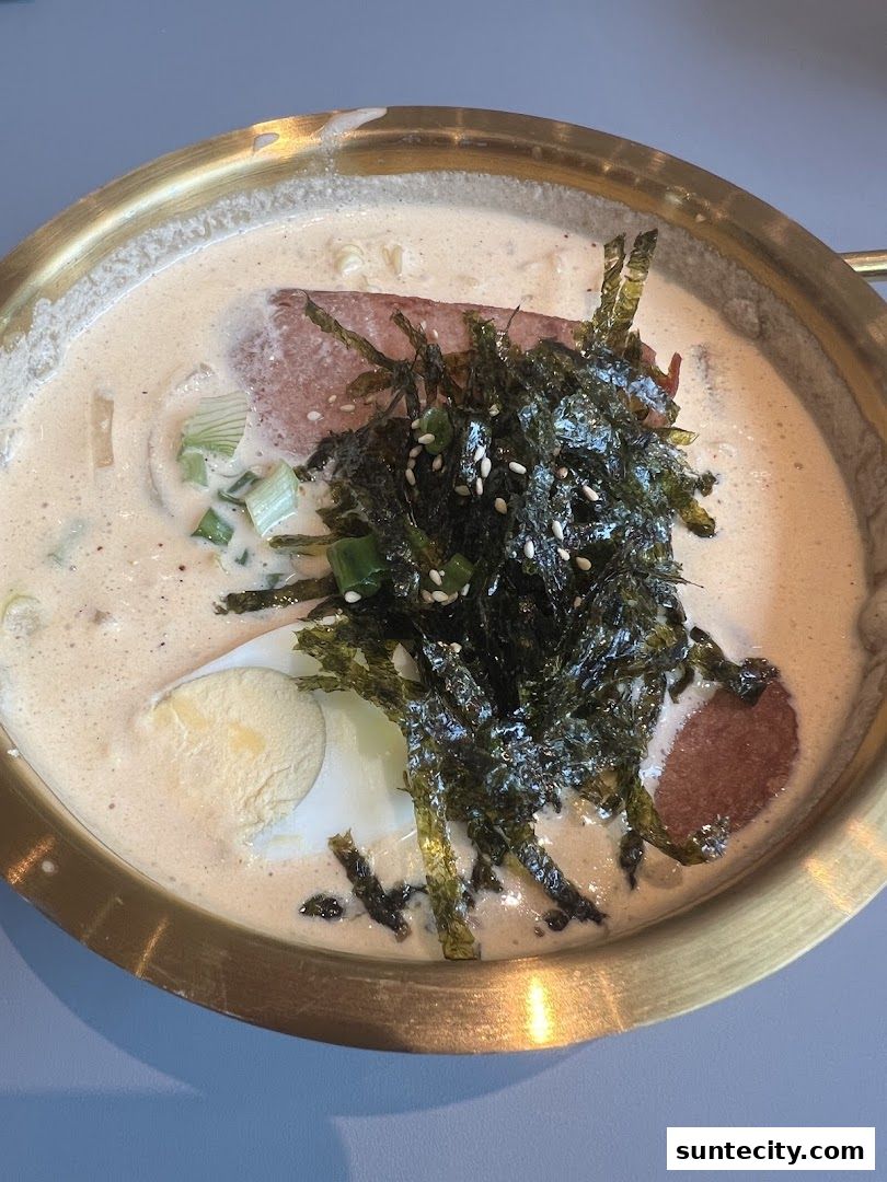 A close-up of a Korean street food dish with broth, noodles, spam, egg, and seaweed.