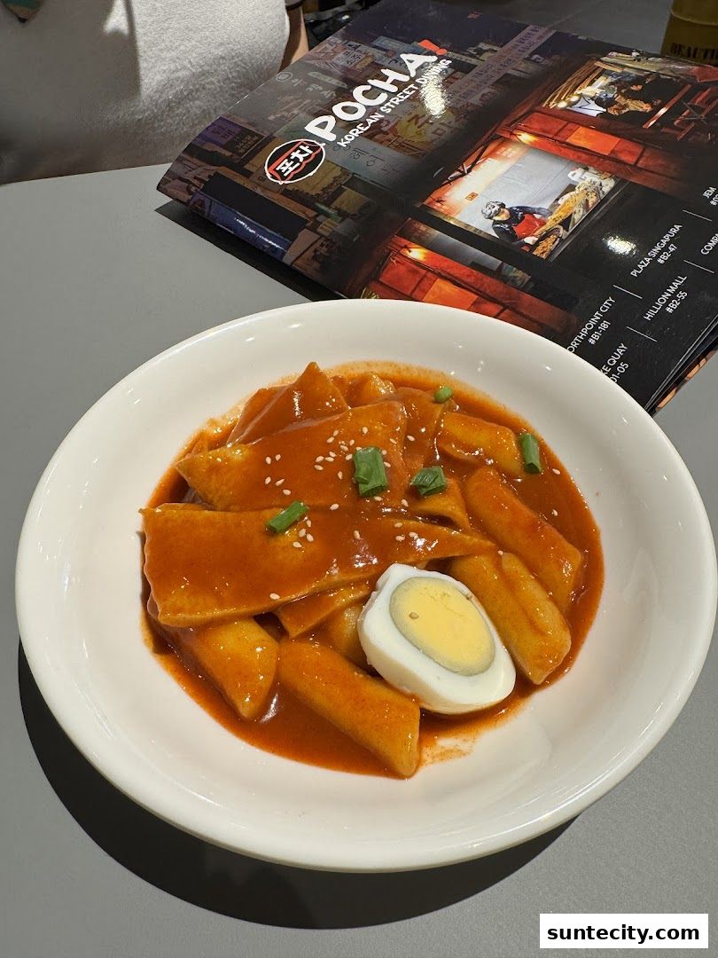 A bowl of Tteokbokki with a hard-boiled egg and a menu from POCHA.