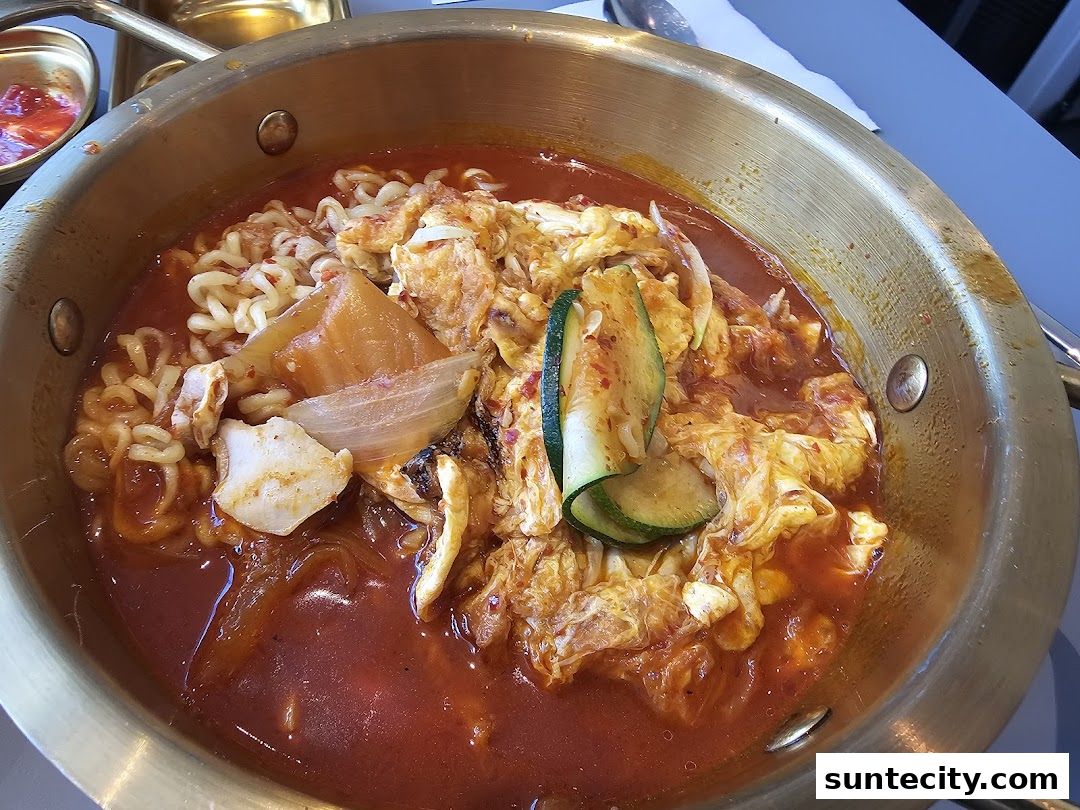 A close-up of a steaming bowl of Korean street food with noodles, egg, and vegetables.