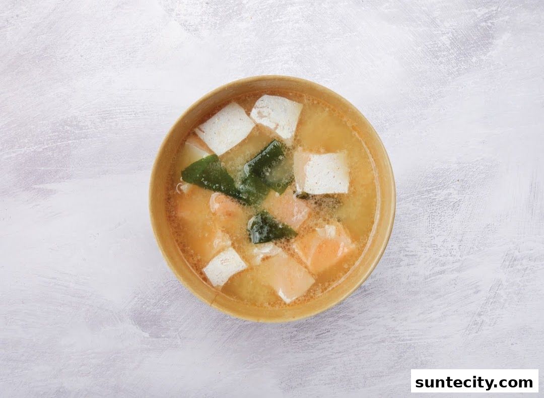 A bowl of miso soup with tofu, seaweed, and salmon pieces.