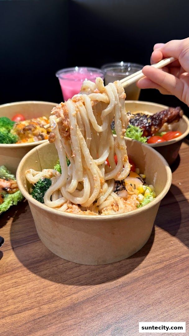 A close-up of a person holding udon noodles with chopsticks from a bowl.