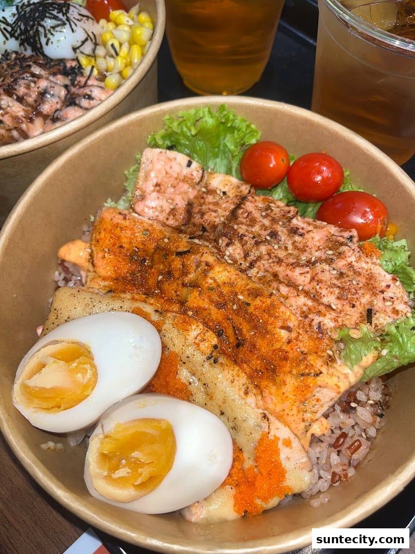 A close-up of a salmon bowl with eggs, cherry tomatoes, and lettuce, served with iced tea.