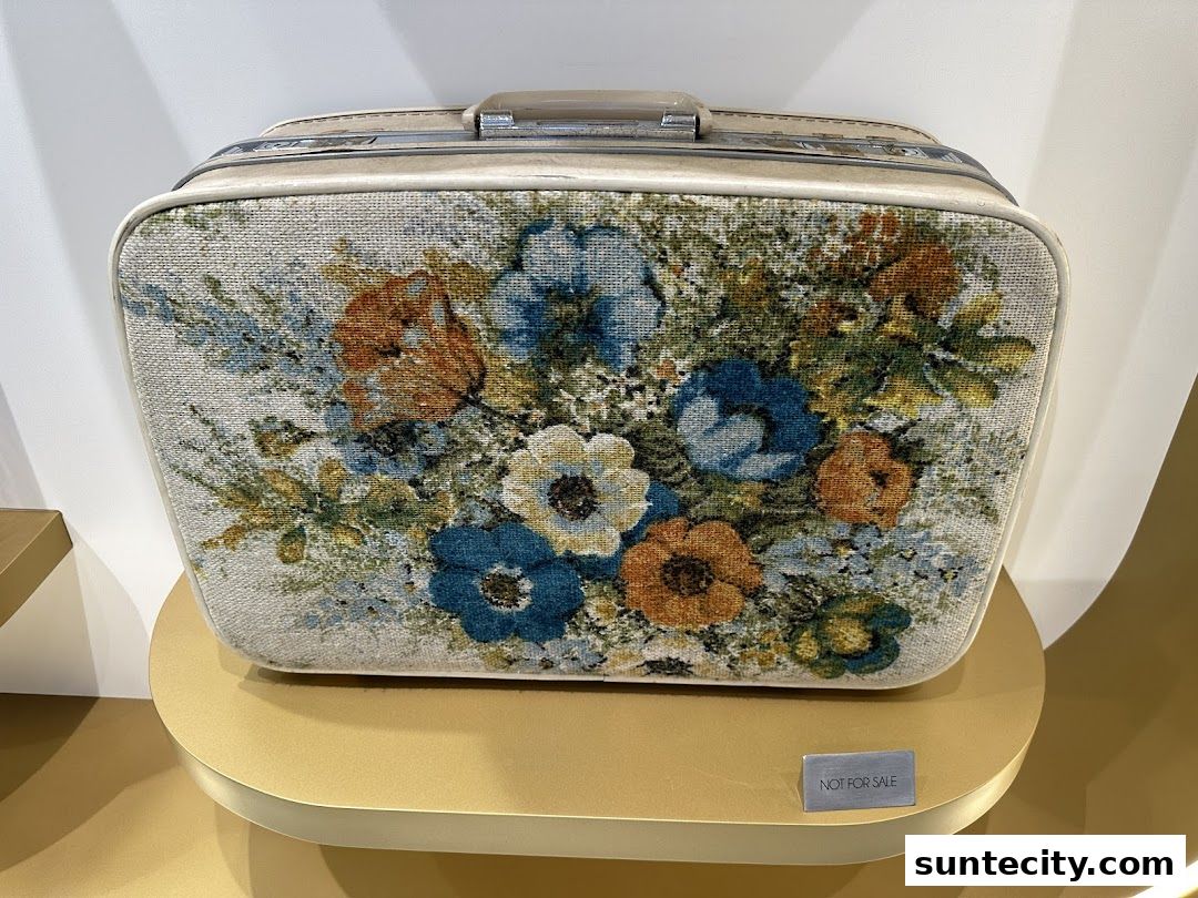 A vintage suitcase with a floral tapestry design displayed on a golden pedestal.