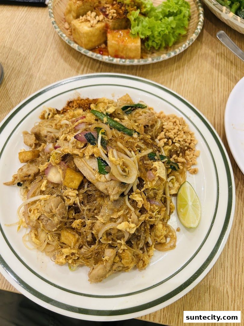 A plate of Pad Thai with chicken, shrimp, and a lime wedge, served with fried tofu and lettuce.