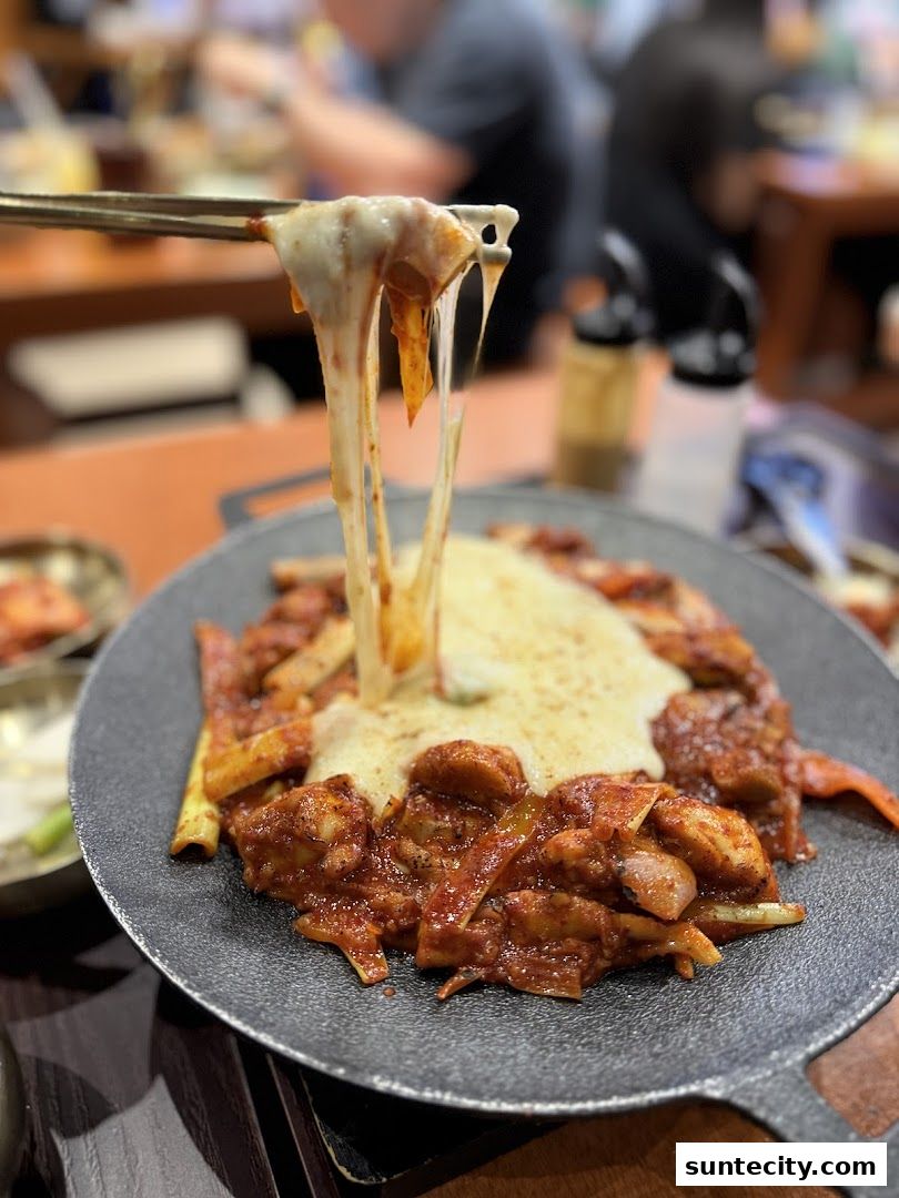 A close-up of cheesy Korean fried chicken being lifted with chopsticks.