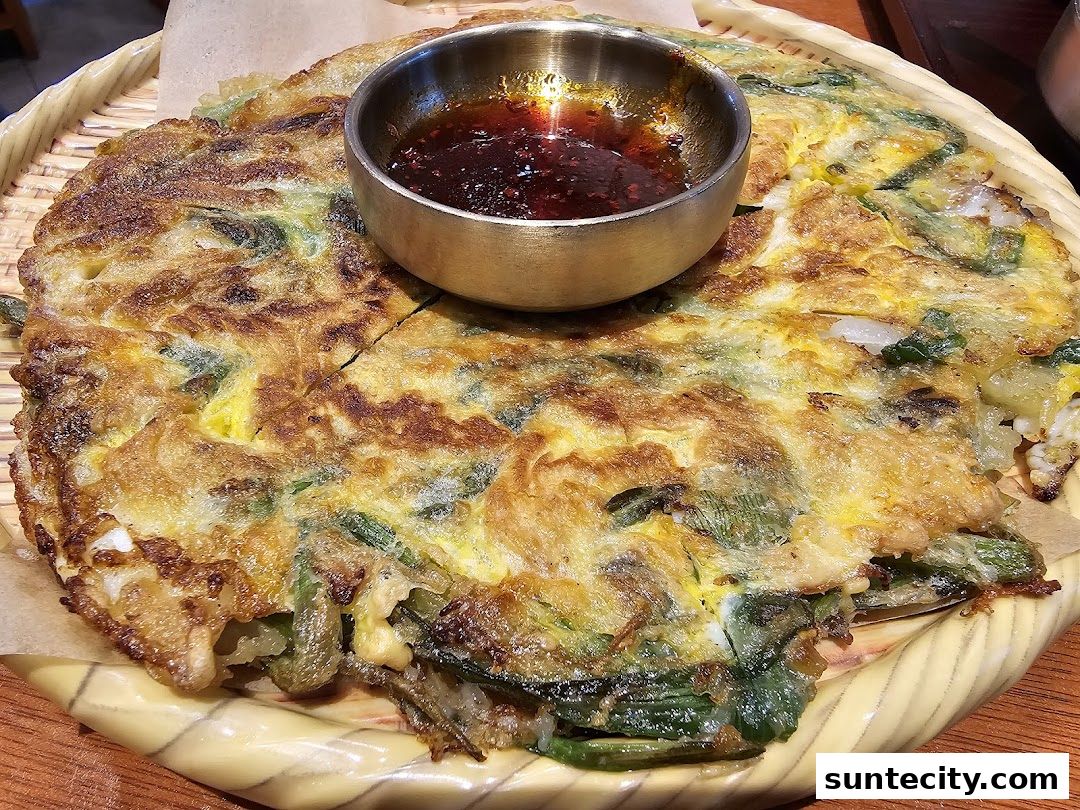 A close-up shot of a savory Korean pancake with a dipping sauce.