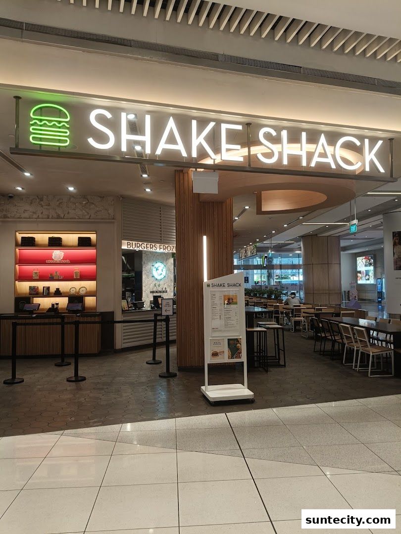 The exterior of a Shake Shack restaurant with its prominent signage and a menu stand.