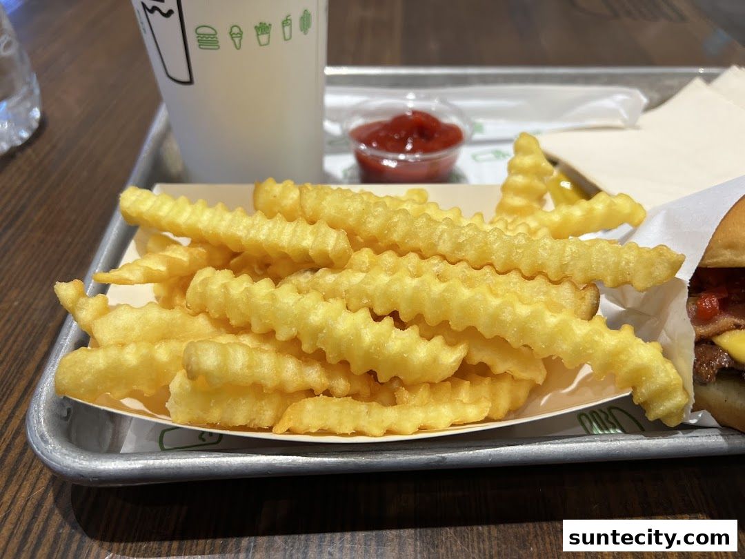 A close-up of crinkle-cut fries, a burger, and a drink from Shake Shack.