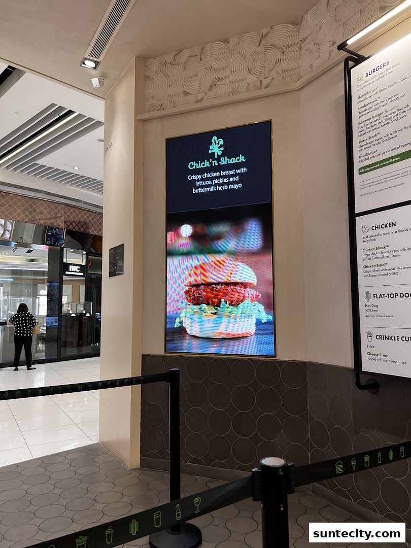 A digital display shows a Chick'n Shack burger next to a menu board.