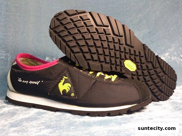 A pair of black Le Coq Sportif sneakers with yellow laces and pink trim.