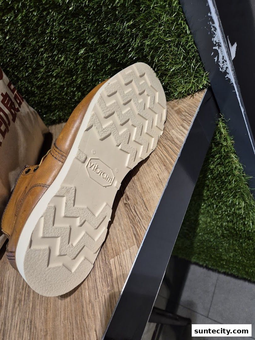 Close-up of a brown leather boot sole with a Vibram logo, on a wooden surface with artificial grass.