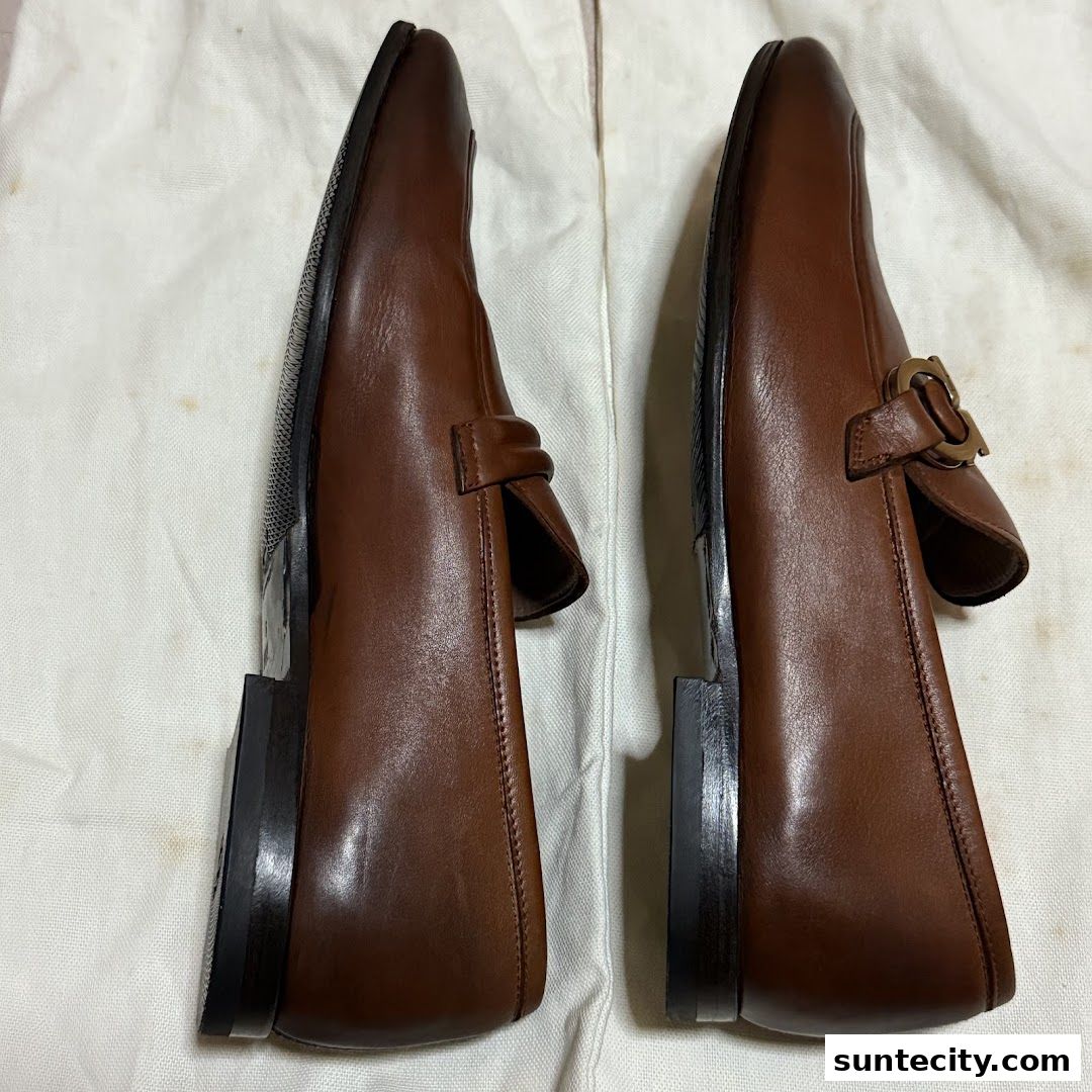 A pair of brown leather loafers with buckle detailing, displayed on a white surface.