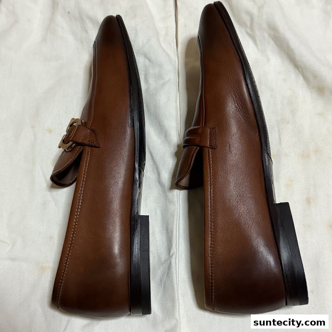 A pair of brown leather loafers with buckle detailing, displayed on a white surface.