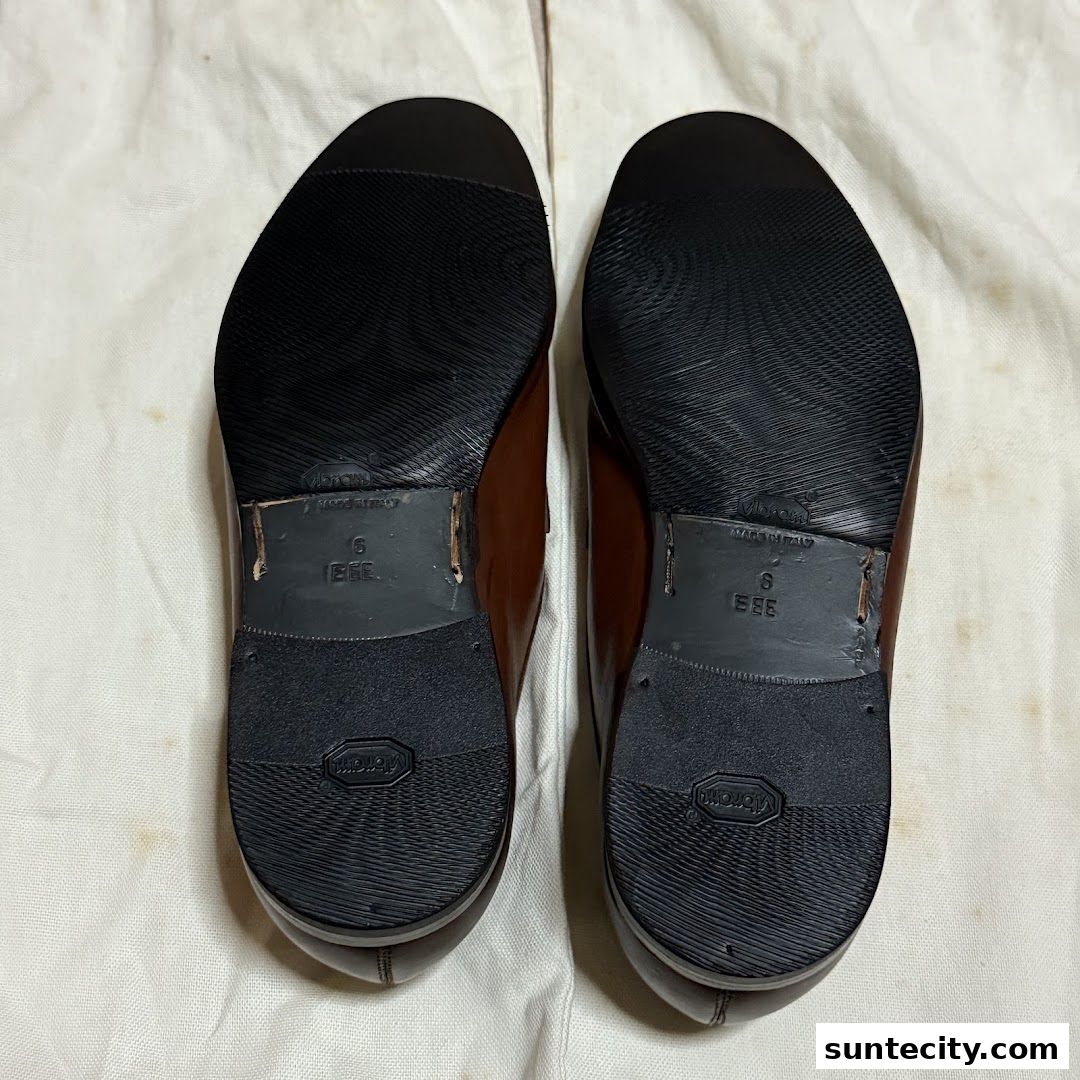 Close-up view of the soles of two brown leather shoes, showcasing Vibram soles and 'Made in Italy' labels.