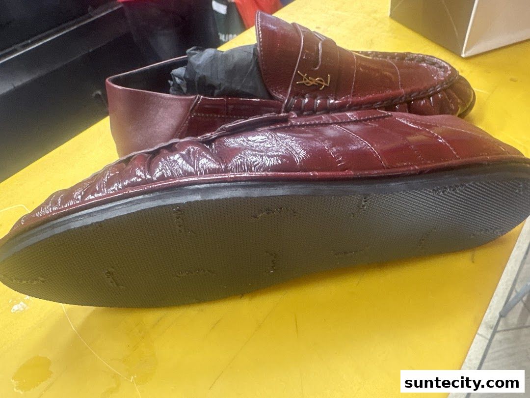 Close-up of shiny burgundy loafers with the YSL logo, displayed on a yellow surface.