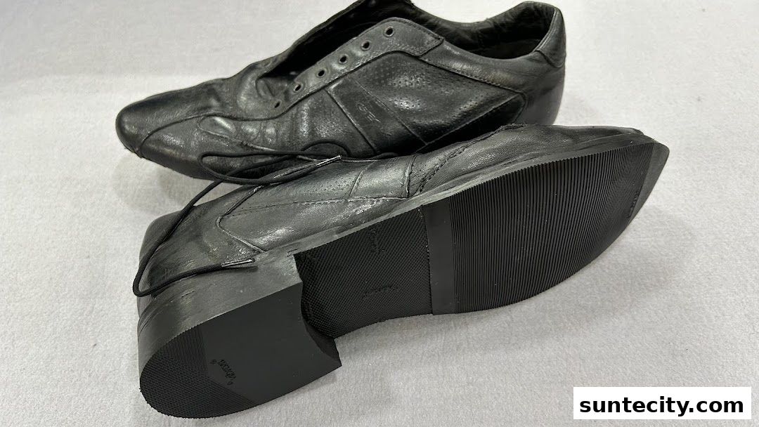 A pair of black leather shoes with laces, displayed on a light gray surface.