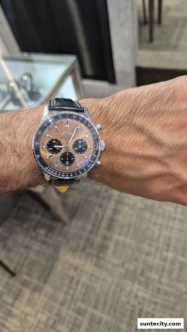 A person's wrist wearing a Breitling Navitimer watch with a rose gold dial.