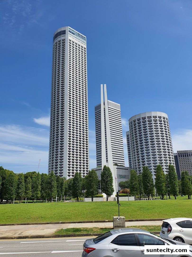 Modern skyscrapers and lush green parkland under a clear blue sky.