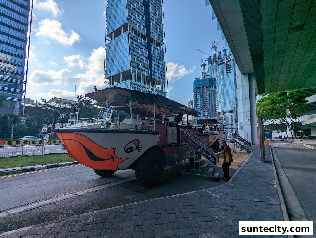 A unique amphibious vehicle with a duck's face painted on the front, parked on a street with skyscrapers in the background.